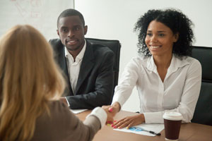 Picture of two smiling people.  one is shaking hands with a third person.